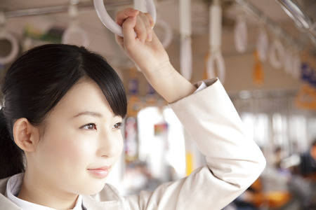 横浜西区保土ヶ谷区神奈川区交通事故むちうち治療に来院するため横浜駅まで電車に乗ってつり革をつかんで立っている女性の写真